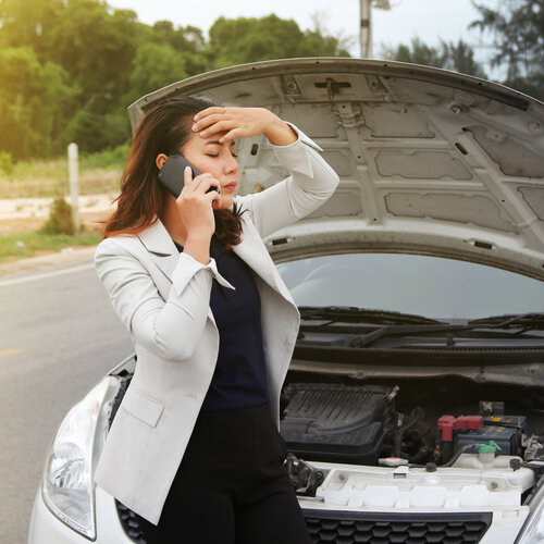 woman next to a broken down car making a phone call