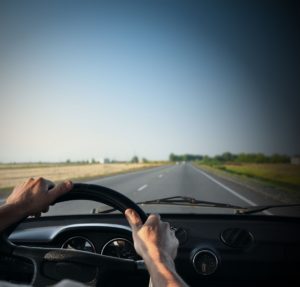 road trip, driver's hands on a steering wheel of a retro car during riding on an empty asphalt road